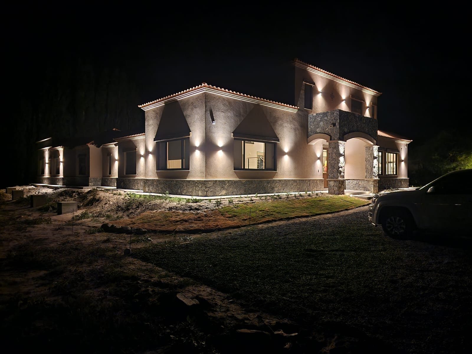 fachada de casa mediterrânea iluminada à noite — projeto Ca La Estancia, por Luciana González Anderson, em Cafayate